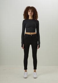Top cropped preto de mangas longas combinado com jeans skinny pretos de cintura alta. Modelo usa tênis brancos. Tecido suave e design ajustado.