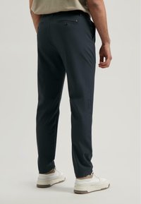 Granatowe spodnie, slim fit, gładki materiał, dwa tylne kieszenie z zapięciem na guziki, połączone z białymi butami sportowymi i szarym topem.