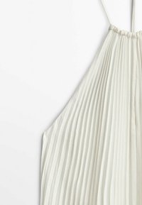 Haut dos-nu en tissu plissé blanc avec fines bretelles et encolure froncée, présenté sur un fond blanc uni.