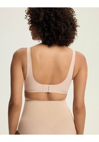 Jasno beżowy stanik z szerokimi ramiączkami, gładką fakturą i zapięciem na haftki. Tył ma niski dekolt i subtelne detale stębnowania.