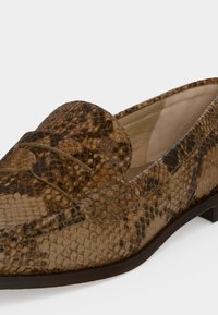 Mocassin en cuir marron imprimé serpent, avec un petit talon, des coutures mocassin et une bride décorative sur le dessus.