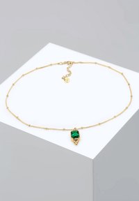 Collar de cadena dorada con un colgante rectangular de gema verde, adornado con pequeñas cuentas redondas a lo largo de la cadena. Cierre ajustable con etiqueta de logo.