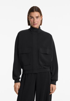 Veste matelassée noire avec un col haut, dotée de deux poches avant, d'un design court et de poignets côtelés. Texture lisse avec un style minimaliste.