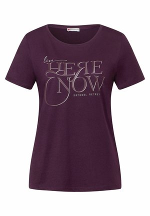 Mørkelilla T-shirt med korte ærmer og rund halsudskæring med sølvtekst, der lyder "live HERE NOW Natural Actrak" på fronten.