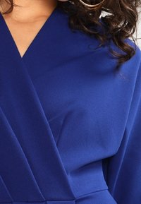 Vestido envolvente azul hecho de tela texturizada, con un escote en V profundo y pliegues estructurados, con un acabado suave y un dobladillo hasta la rodilla.