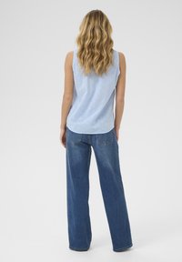 Un haut sans manches bleu clair avec un motif texturé, associé à un jean bleu foncé ample. La tenue présente une silhouette décontractée.