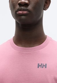 T-shirt en coton rose clair avec un col rond et un petit logo gris sur la poitrine. Texture lisse avec des manches courtes.