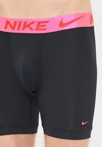 Schwarze Boxerbriefe mit einem pinken Nike-Logo-Bund und kleinem pinken Swoosh am Bein, aus glattem, dehnbarem Stoff und mit figurbetontem Design.