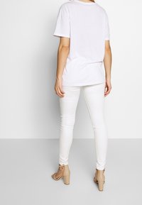 Camiseta blanca de manga corta, combinada con jeans ajustados blancos y sandalias de tacón cuadrado beige. La tela parece suave y ligera.