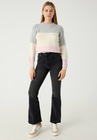 Suéter ligero en rayas grises, crema y rosa; combinado con jeans acampanados de tiro alto en negro y zapatillas crema con acentos en beige.