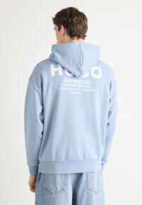 Lichtblauw hooded sweatshirt met ribgebreide manchetten en zoom, met een groot wit logo en tekst op de achterkant, textiel met structuur.