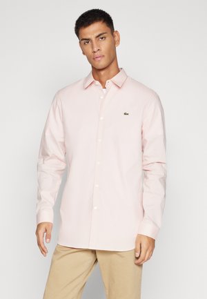 Camisa de botones rosa claro hecha de algodón, con un logo bordado verde en el pecho, mangas largas y diseño de cuello clásico.