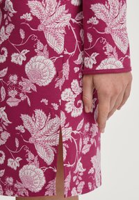 Vestito fucsia con un motivo floreale bianco, maniche lunghe e una fessura laterale. Il tessuto ha una consistenza liscia con un design aderente.