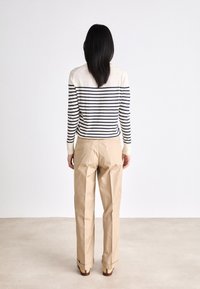 Sweter w paski w kolorze kremowym i granatowym, zestawiony z beżowymi spodniami. Stylizacja charakteryzuje się luźnym krojem oraz mankietami przy rękawach i nogawkach.