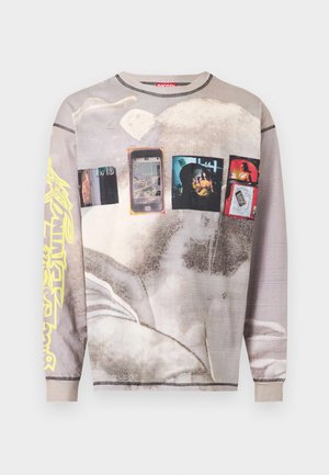 Chemise beige délavée à manches longues avec des imprimés graphiques de smartphones, de personnes et de formes abstraites, avec un design de texte jaune sur une manche.