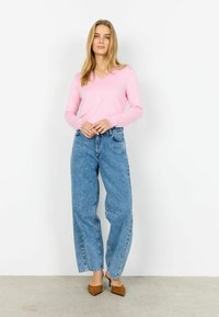 Hele-roosa pika varrukaga särk V-kaelusega ja pitsdetailidega, millele on lisatud kõrge vöökohaga lahtised helesinised teksapüksid ja pruunid kõrged kontsad.