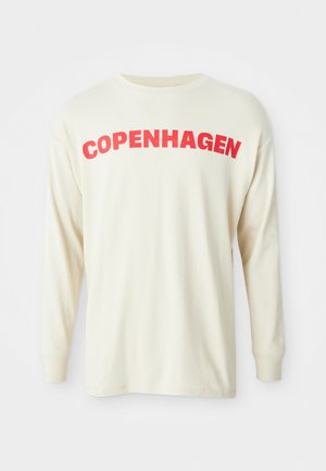 Långärmad krämfärgad t-shirt i bomull med fet röd text som säger "KÖPENHAMN" över bröstet. Rund halsringning och uppvikta ärmar.