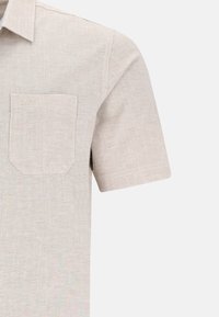 Ljust beige kortärmad skjorta i texturerad tyg; har en vänster bröstficka med en subtil logotyp, rena linjer och sydda detaljer.