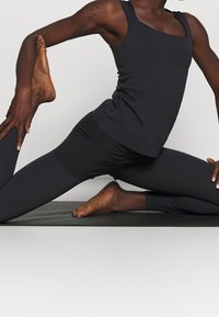 Black athletic tank top with a square neckline, paired with black leggings. The fabric appears smooth and stretchy.êmes stretch and comfort.