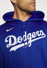 Sweat à capuche bleu Nike avec un grand logo "Dodgers" blanc. Comprend une capuche à cordon de serrage et un tissu texturé. Design épuré sans motifs supplémentaires.