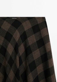 Jupe trapèze à carreaux noirs et marrons avec une texture subtile, montrant la ceinture et une partie de la partie supérieure de la jupe.