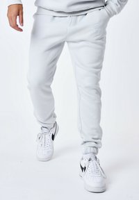 Lichtgrijze joggerbroek met elastische boorden en een koordje in de taille. Witte sneakers met zwarte accenten maken de outfit af.