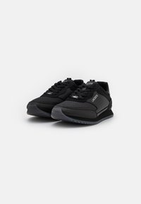 Schwarze Sportschuhe mit einem strukturierten Mesh-Obermaterial, glatten synthetischen Akzenten, gepolstertem Schaftrand und Gummisohle mit einem subtilen Profil.