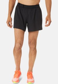 Black athletic shorts with an elastic waistband, smooth texture, and a subtle pattern. Paired with bright orange running shoes.