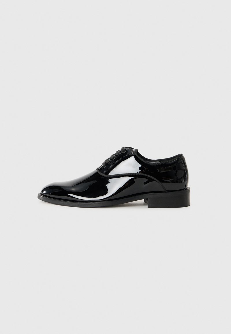 Chaussure habillée en cuir verni noir avec un bout arrondi, un laçage et un petit talon carré. Texture lisse avec une finition brillante.