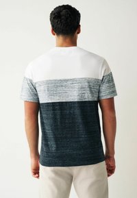 Herre kortærmet t-shirt med farveblokdesign: hvid, lys grå, mørk grå og marineblå. Blødt, tekstureret stof med rund halsudskæring.