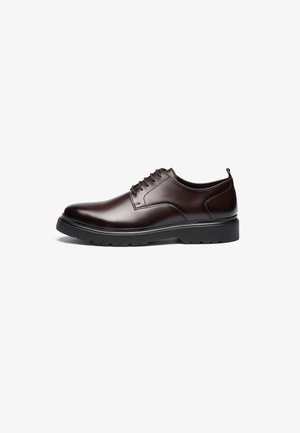 Scarpa in pelle marrone con lacci, dal design elegante, punta rotonda, suola in gomma nera a contrasto e cuciture minime visibili.