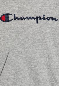 Šedá mikina s kapucí a přední kapsou, s vyšitým logem "Champion" v modré a červené barvě. Měkká textura a ležérní design.