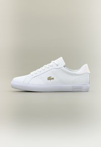 Bijele kožne patike s glatkom teksturom, zlatnim naglascima, perforiranim detaljima i ravnim bijelim gumiranim đonom.