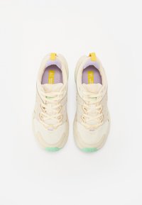 Beige Sport Schuhe mit einer atmungsaktiven Mesh-Oberfläche, lila und grünen Akzenten, einem gemusterten Sohle und einem gelben Zugband an der Ferse.