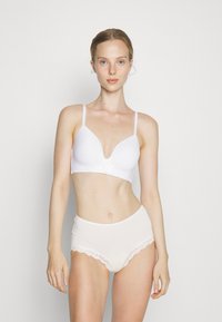 Sutiã sem fios branco com decote em V profundo, apresentando detalhes florais ao centro, combinado com cuecas brancas de cintura alta com rendas.