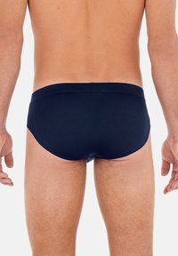 Dunkelblaue Herren-Schwimmslips mit glatter Textur und elastischem Bund, die eine enge Passform und minimalistisches Design aus der Rückansicht zeigen.