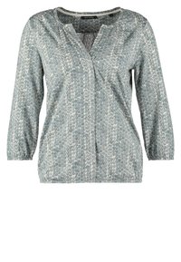 Blouse gris clair à manches longues avec encolure ronde et petit motif à pois dans des tons gris plus foncés, avec une courte patte de boutonnage.