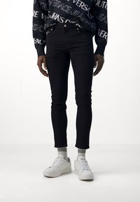 Jeans skinny negros con textura de mezclilla, combinados con zapatillas blancas. Incluyen un corte ajustado y discretos acentos en dorado.