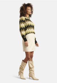 Black and green zigzag patterned sweater, beige button-front mini skirt, and beige slouchy knee-high boots. Smooth texture, fitted design.