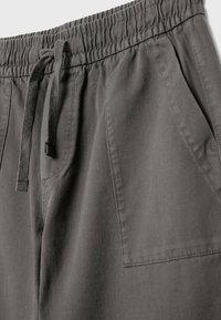 Lähiotos harmaista joustavista vyötäröstä, joissa on nyörikiinnitys ja näkyvät sivutaskut pehmeästä kankaasta.