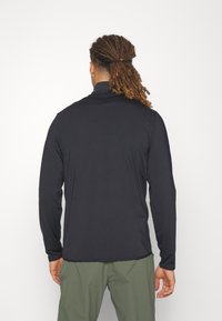 Herrskjorta med långa ärmar i svart, tillverkad av mjukt tyg, med en ståkrage och en figursydd design. Bakifrån visas minimala sömnadsdetaljer.