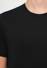Fekete póló, puha és rugalmas anyagból készült. Kerek nyakkivágással és rövid ujjal rendelkezik, sima tapintású, látható logók nélkül.