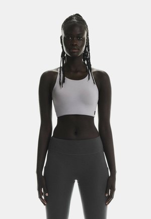 Witte cropped sportbeha met een ronde halslijn, gecombineerd met high-waisted donkergrijze leggings, beide gemaakt van een zachte, elastische stof.