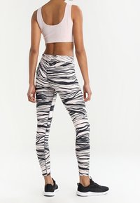 Ljust rosa sportbh med perforerade detaljer, tillsammans med högmidjade leggings med ett mönster av svart och creamfärgad zebrastripe.