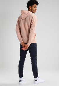 Felpa rosa chiaro in cotone con vestibilità comoda, abbinata a pantaloni blu navy scuri. La felpa presenta un cappuccio regolabile e polsini a coste.