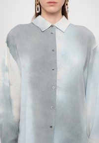 Camicia button-up azzurro chiaro e grigia con tessuto morbido e testurizzato. Presenta un colletto classico e bottoni argentati sul davanti.