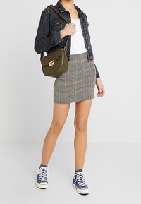 Spijkerjack, wit topje, beige-zwart geruite minirok, blauwe canvas sneakers, olijfgroene schoudertas met gespdetail.