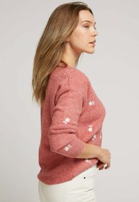 Pull en laine rose avec de délicates broderies florales blanches sur les manches, avec des poignets et un ourlet côtelés. Texture lisse, coupe décontractée.