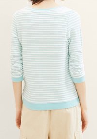 Ljusblå randig tröja med rund halsringning och trekvartsärmar. Har ribbade muddar och nederkant, tillverkad av mjukt tyg.