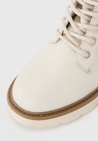 Bota alta de cuero blanco con punta redonda, cordones crema y suela de goma marrón. Presenta ojales metálicos y costuras texturizadas.